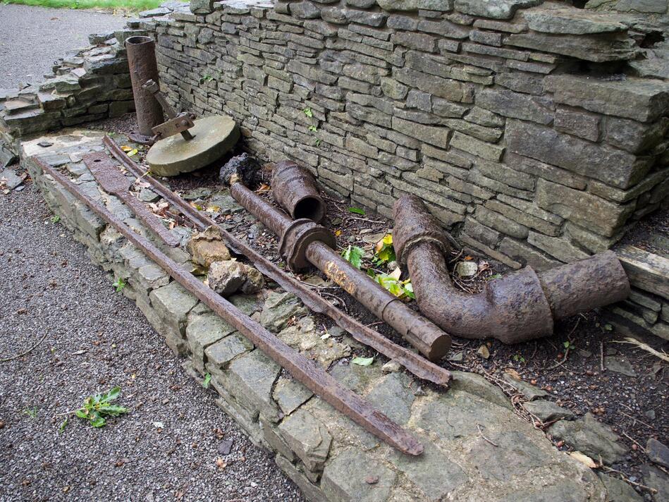 Rusted pieces of a machine laid at the foot of a brick wall.